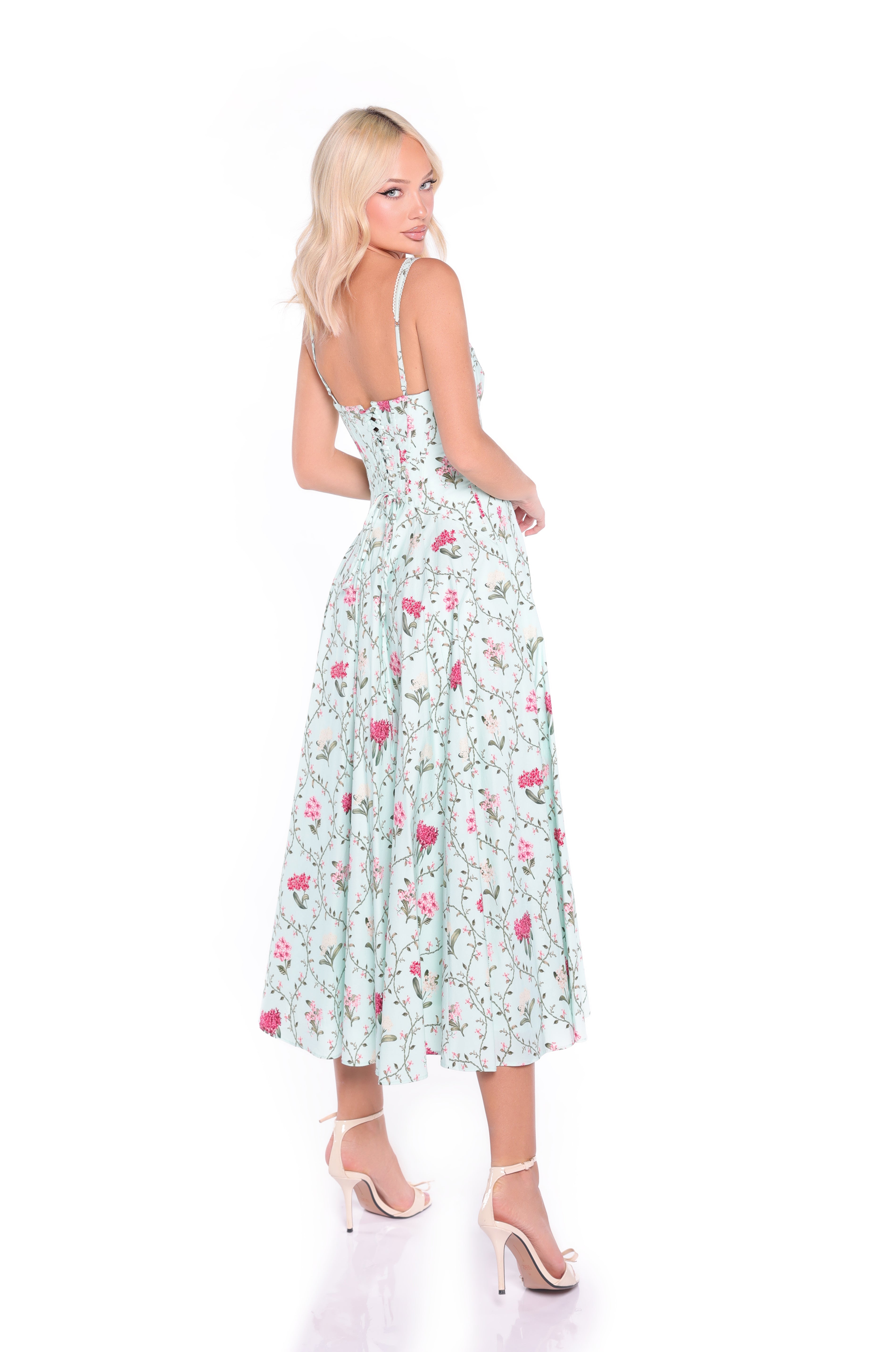 A woman in the Rosella Mint Green Floral Casual Midi Dress poses over her shoulder, wearing white high-heeled sandals against a white background.